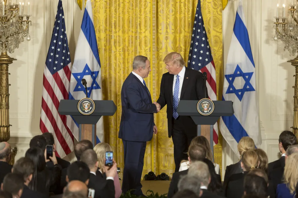 Benjamin Netanyahu and Donald Trump shake hands at joint press conference with U.S. and Israeli flags, as Netanyahu defends Trump’s Gaza plan.